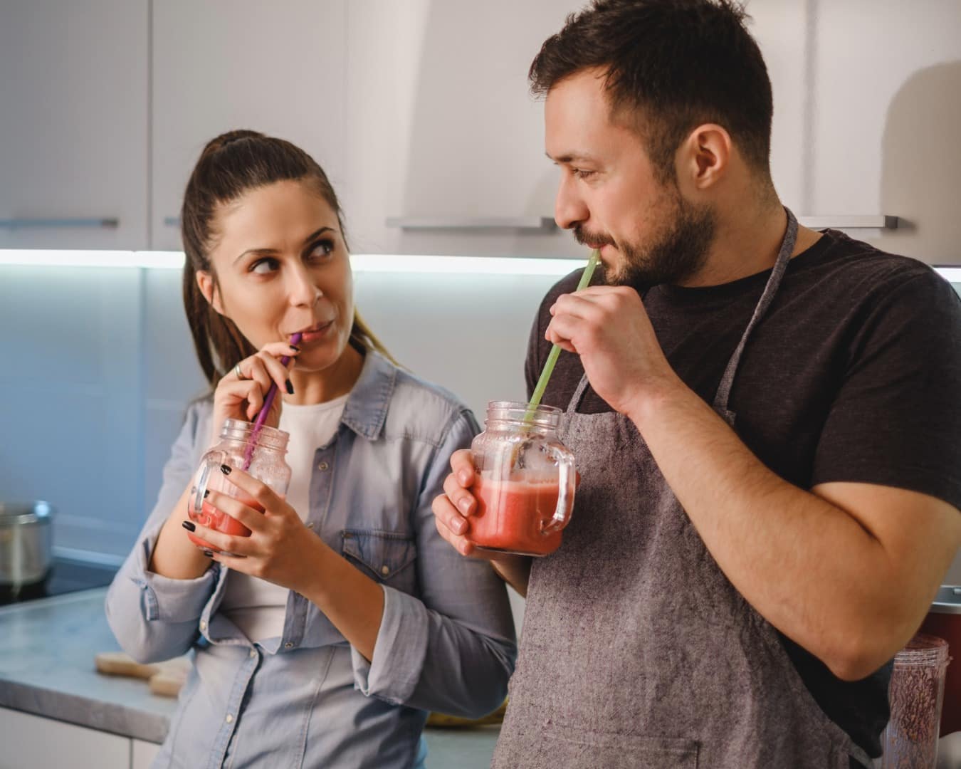 Mann und Frau flirten in der Küche, während sie einen Proteinshake trinken.