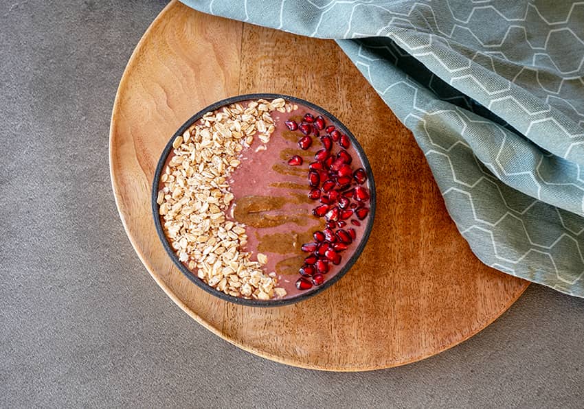 Frucht-Nuss-Smoothie mit angekeimten Haferflocken, Erdmandelcreme und Granatapfelkernen in einer Schüssel angerichtet