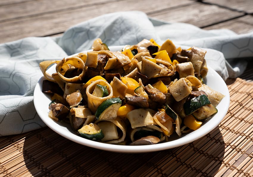 Calamarata mit mediterranem Gemüse mit sichtbaren Paprika, Zucchini und Auberginenstücken in einem tiefen Teller angerichtet.